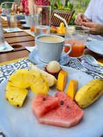 A dining table with a plate of fruit, a cup of coffee, and a glass of juice.