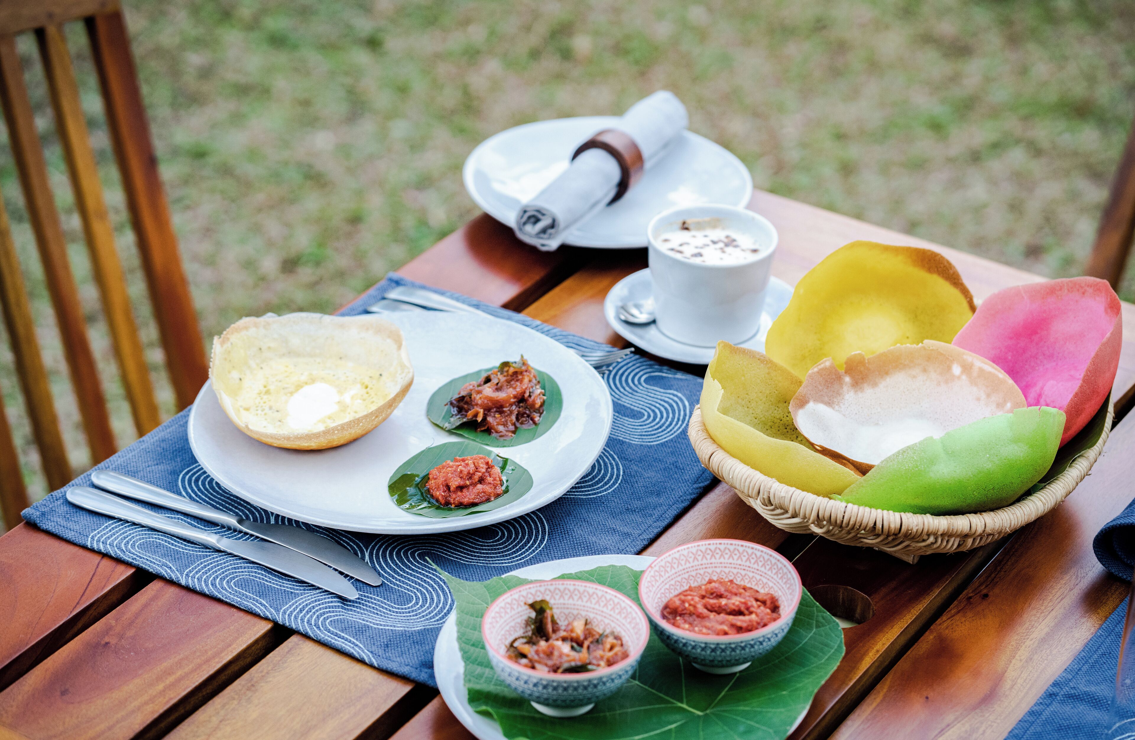 A table set with a plate of food, a cup of coffee, and a basket of colorful items.
