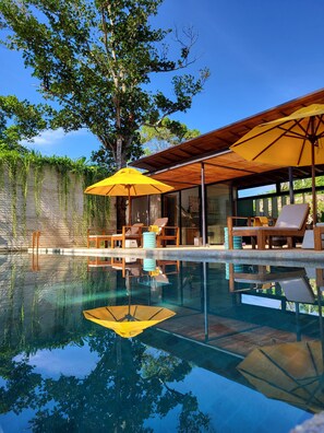 A pool area with lounge chairs and umbrellas, surrounded by trees and a wooden pergola. - Villa Alba (Ahangama)