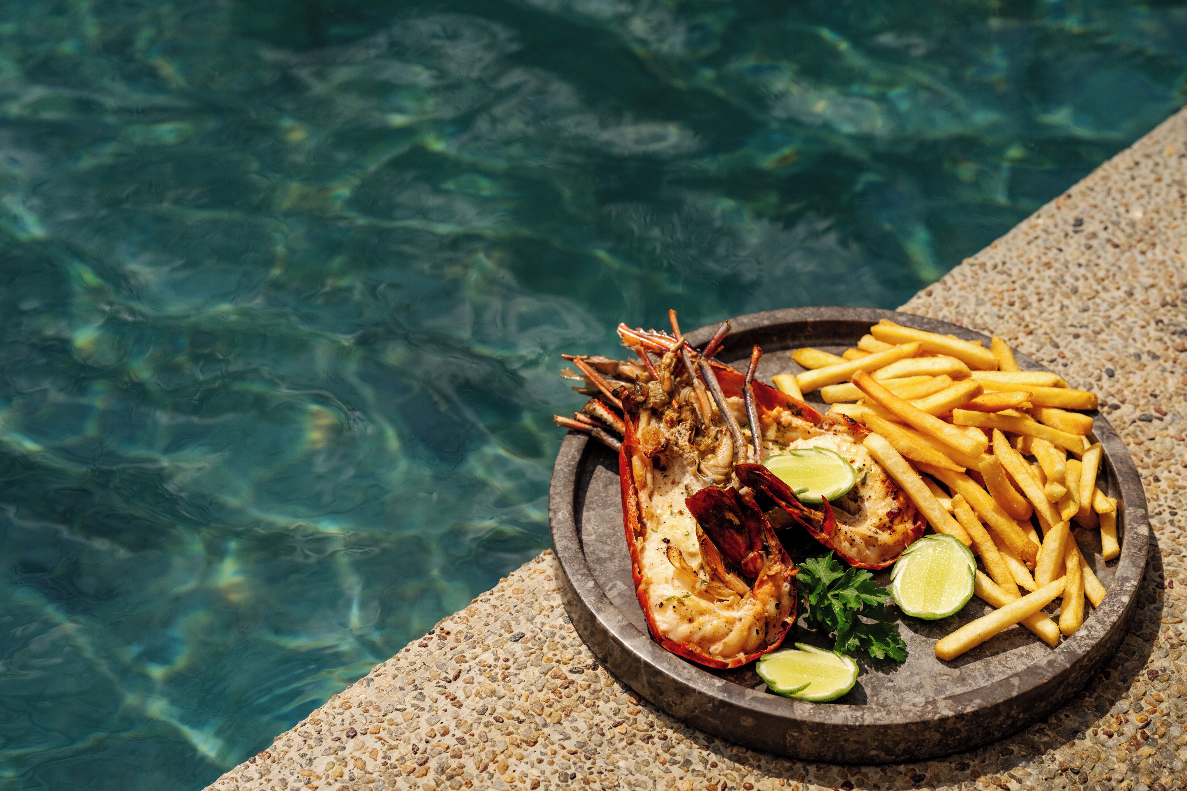 A seafood platter with shrimp, fries, and lime on a stone table by a pool.