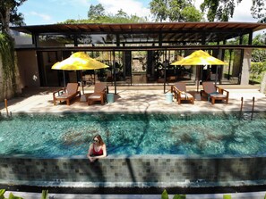 Una piscina al aire libre, sombrillas, sillones reclinables de piscina