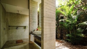 A modern bathroom with a large bathtub, a shower, and a sink. There is a stone wall and a small garden area with plants. - Villa Alba (Ahangama)