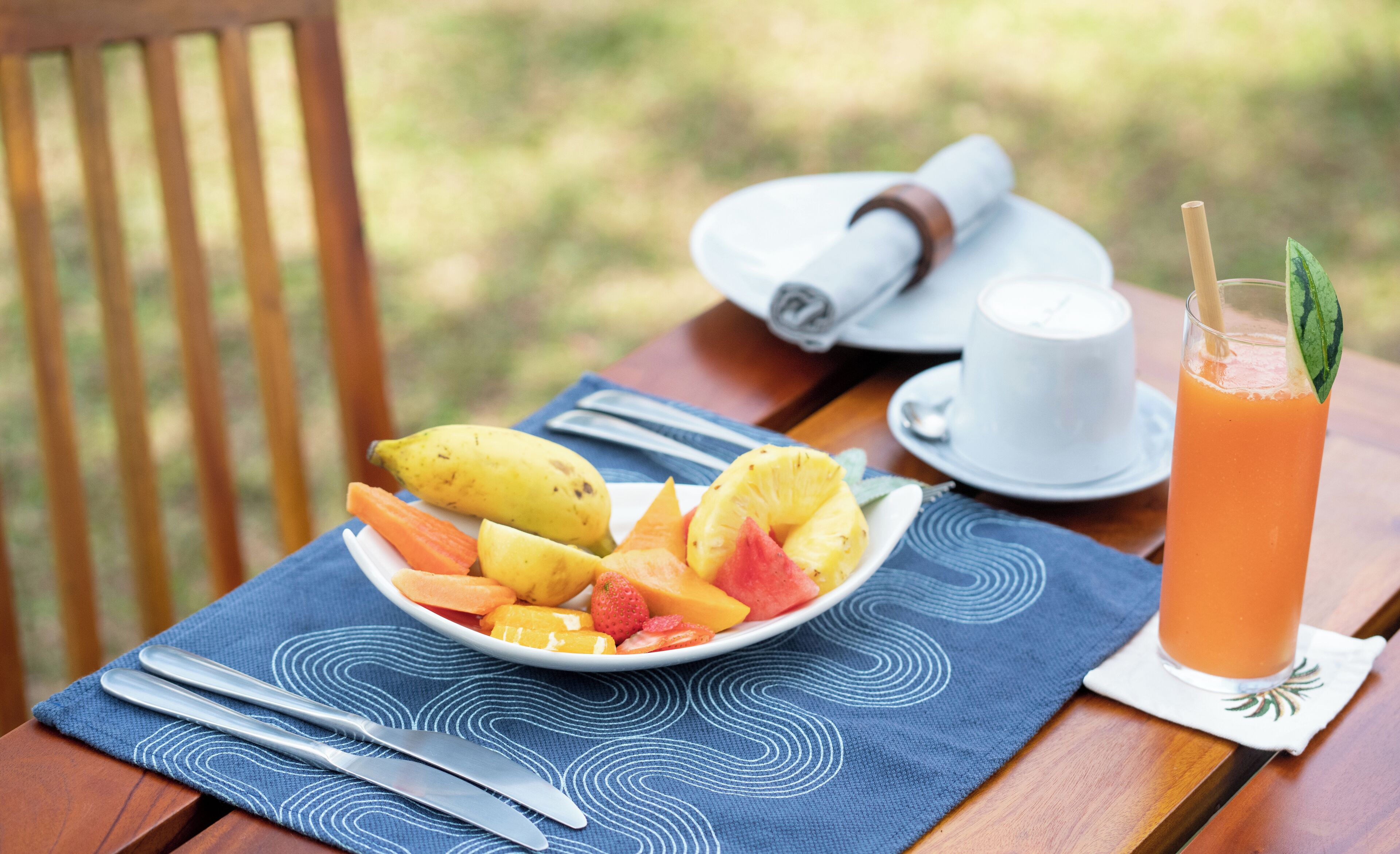 A wooden table with a plate of fruit, a glass of orange juice, and a cup of coffee.