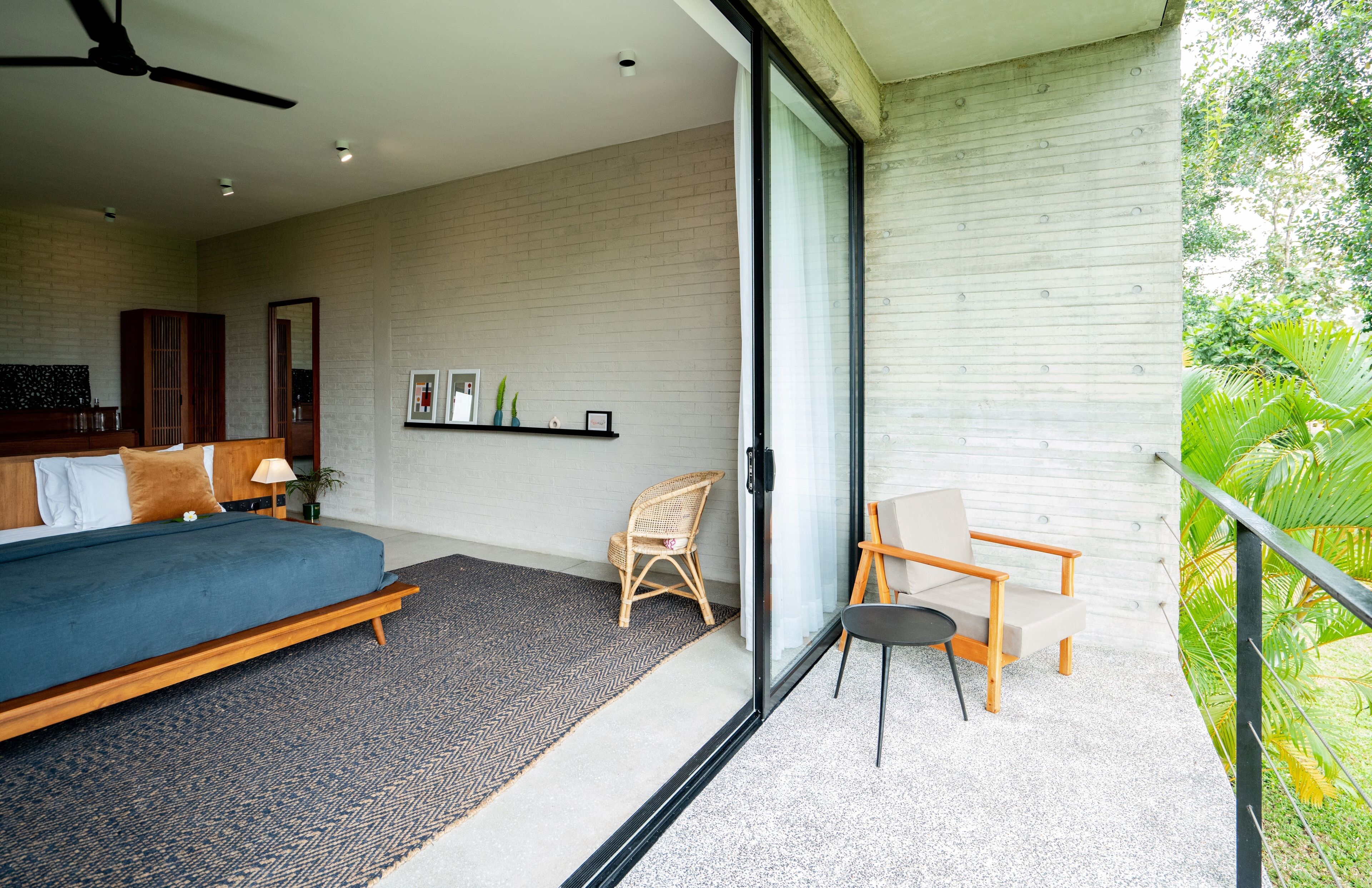 A modern bedroom with a bed, a chair, a small table, and a balcony with a view of greenery.