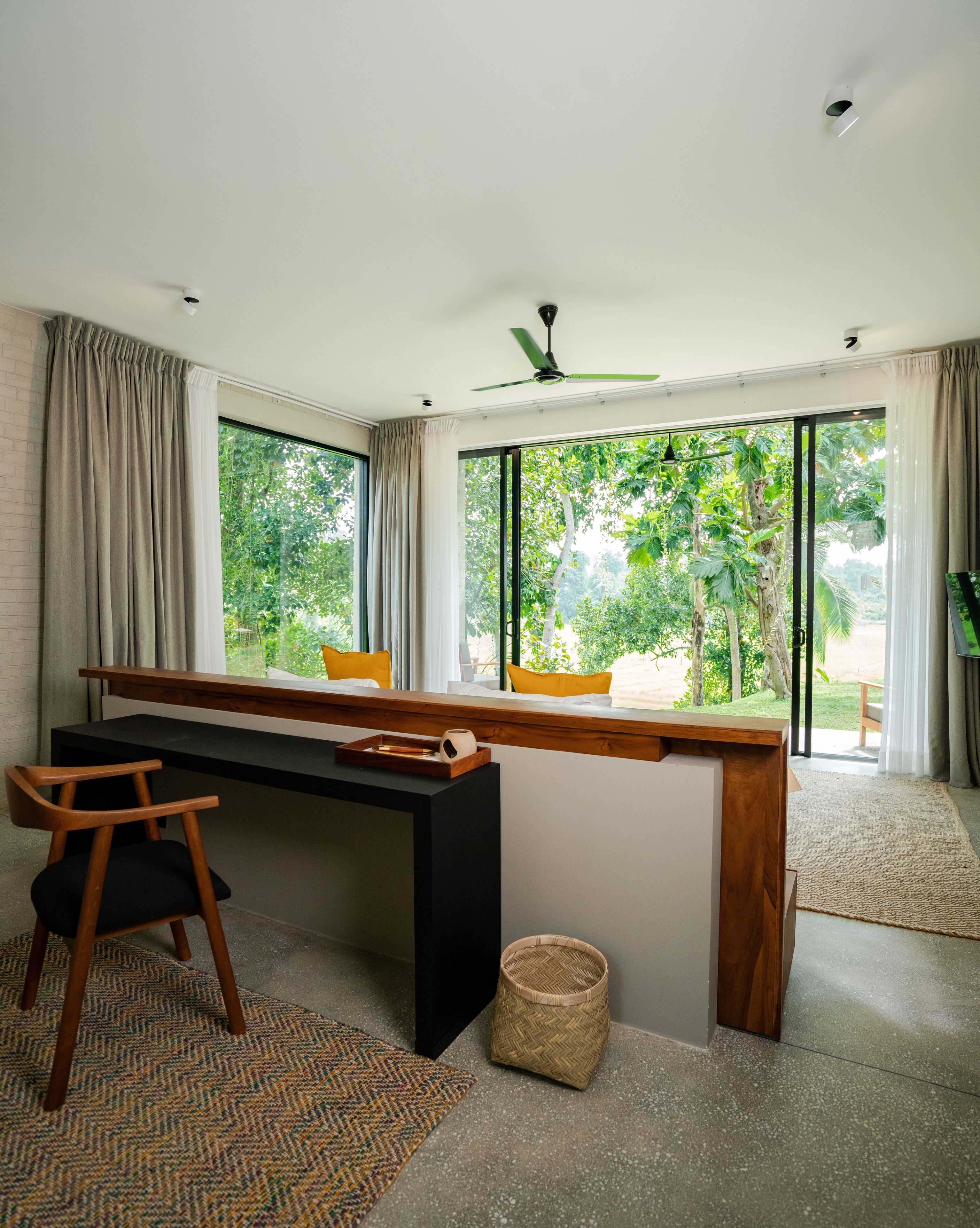 A modern room with a large window, a desk, a chair, and a ceiling fan.