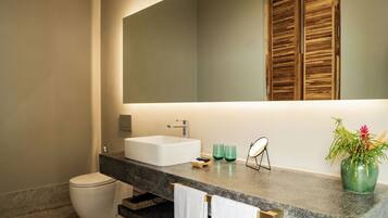 A modern bathroom with a large mirror, a white sink, and a toilet. There are two towels hanging on the towel bar, and a potted plant on the counter.