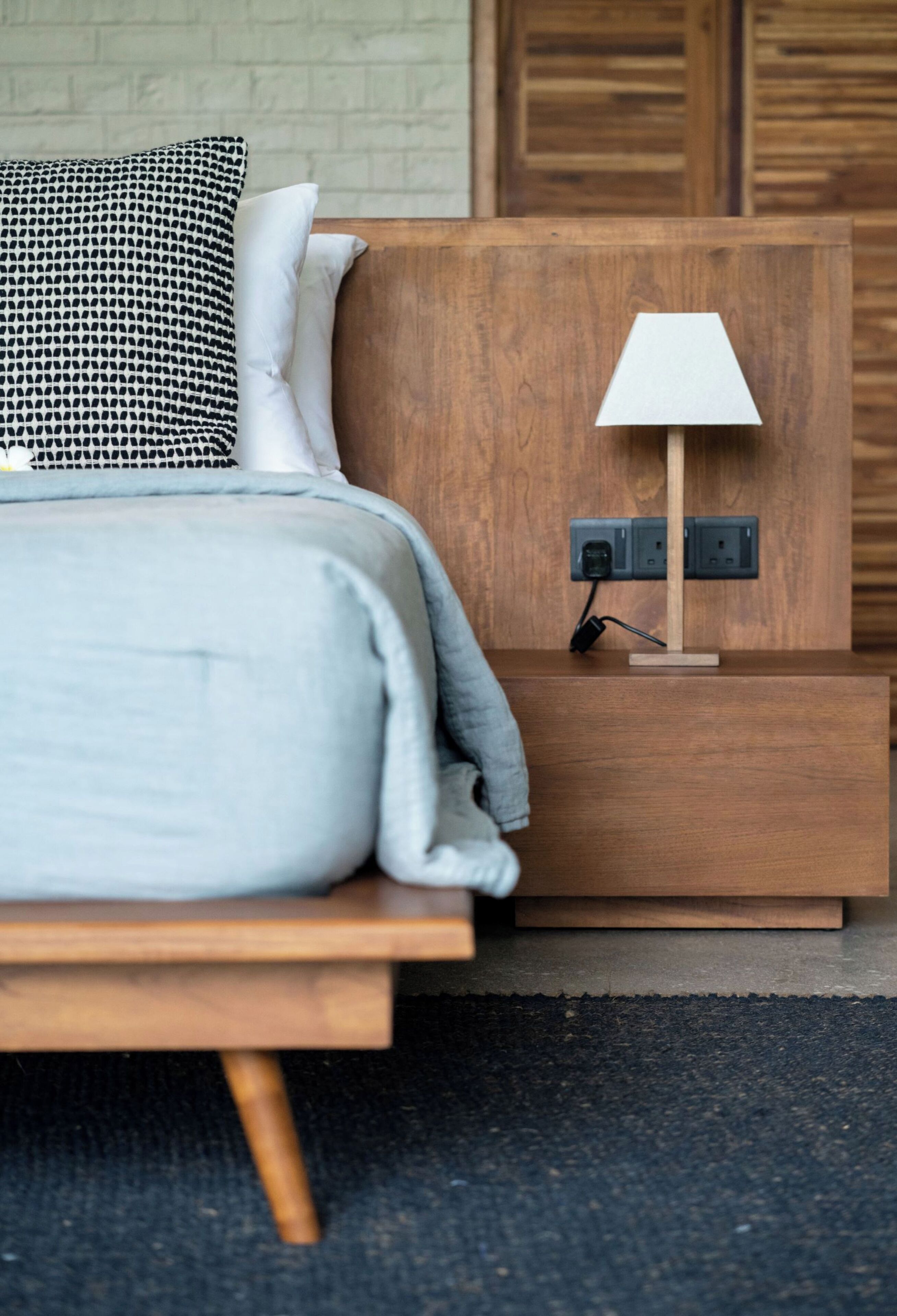 A modern bedroom with a wooden headboard, a bedside table with a lamp, and a power outlet.