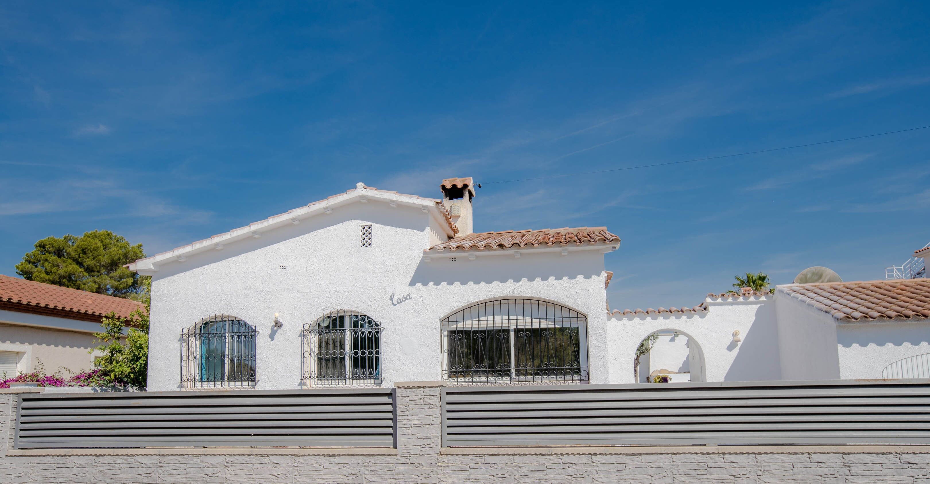 A white building with a tiled roof, a chimney, and a gated entrance.