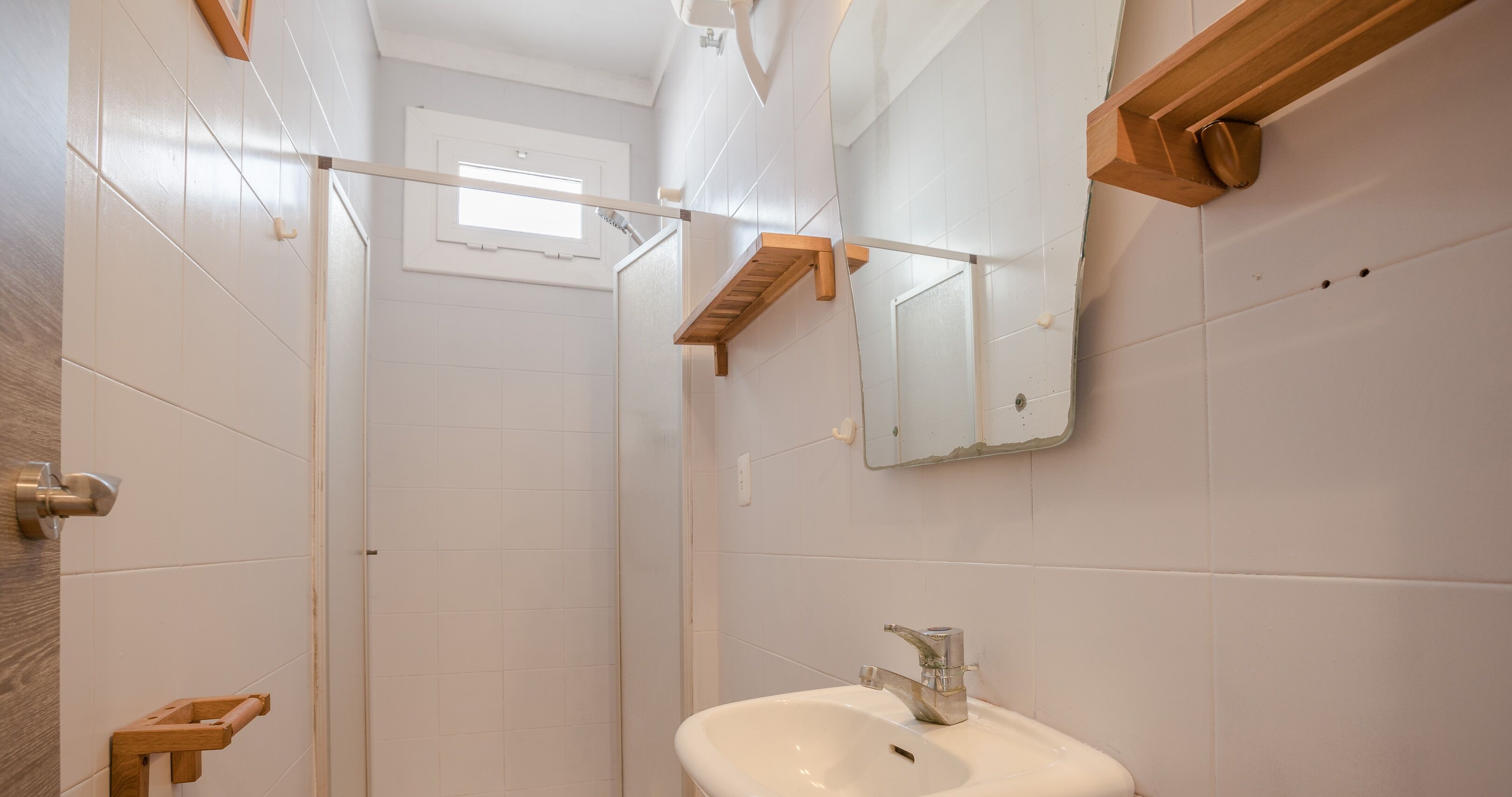 Un baño con azulejos blancos, un estante de madera, un espejo y un lavabo.