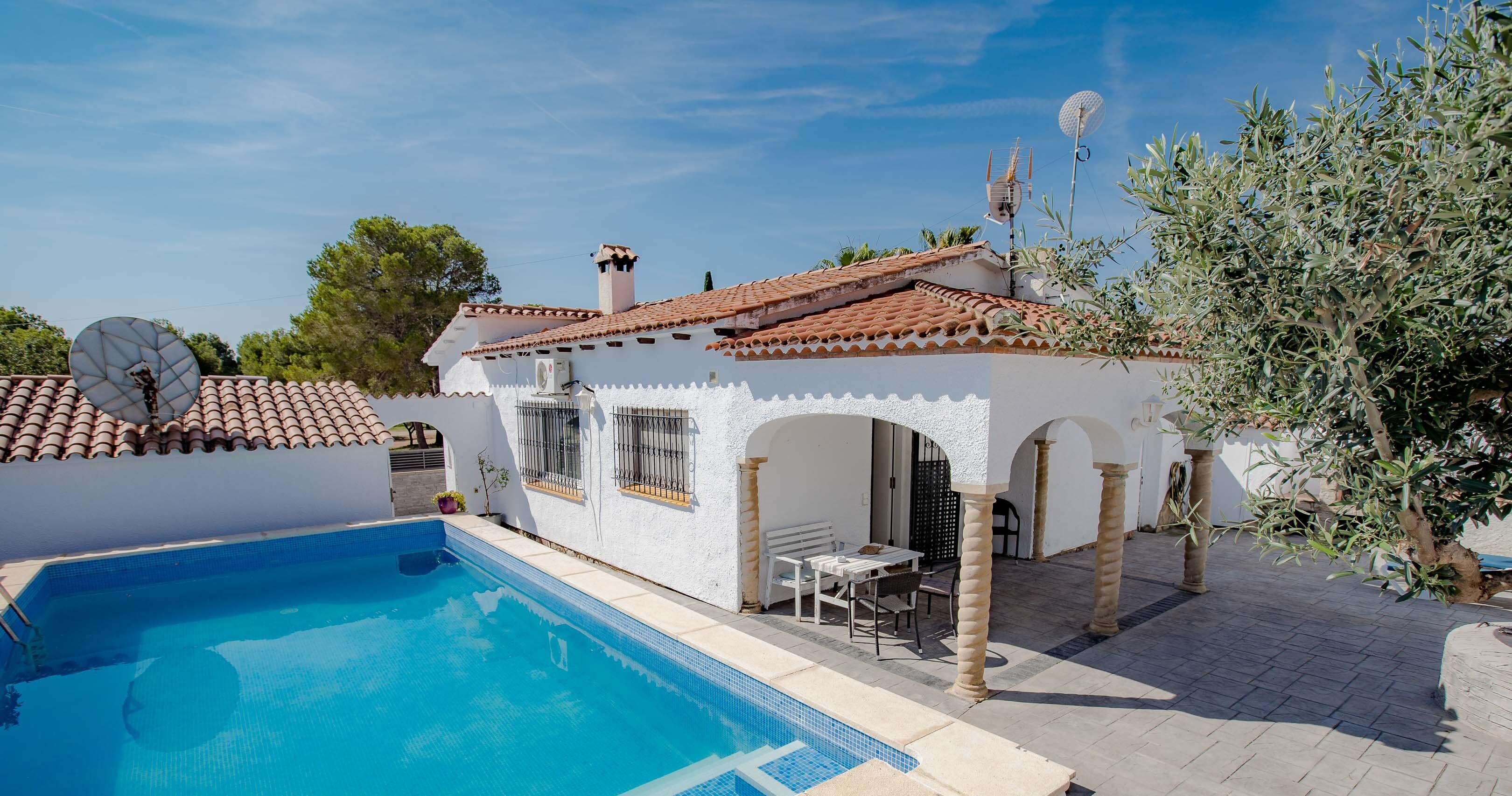 Una villa blanca con techo de tejas, piscina y mobiliario exterior.