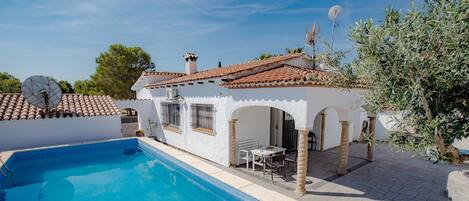 Una villa blanca con techo de tejas, piscina y mobiliario exterior.