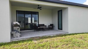 Una veranda coperta con un'area salotto, una ventola a soffitto e un barbecue.
