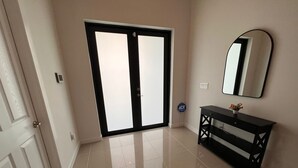 Una stanza con una porta doppia, un tavolo consolle nero con uno specchio e un pavimento piastrellato.
