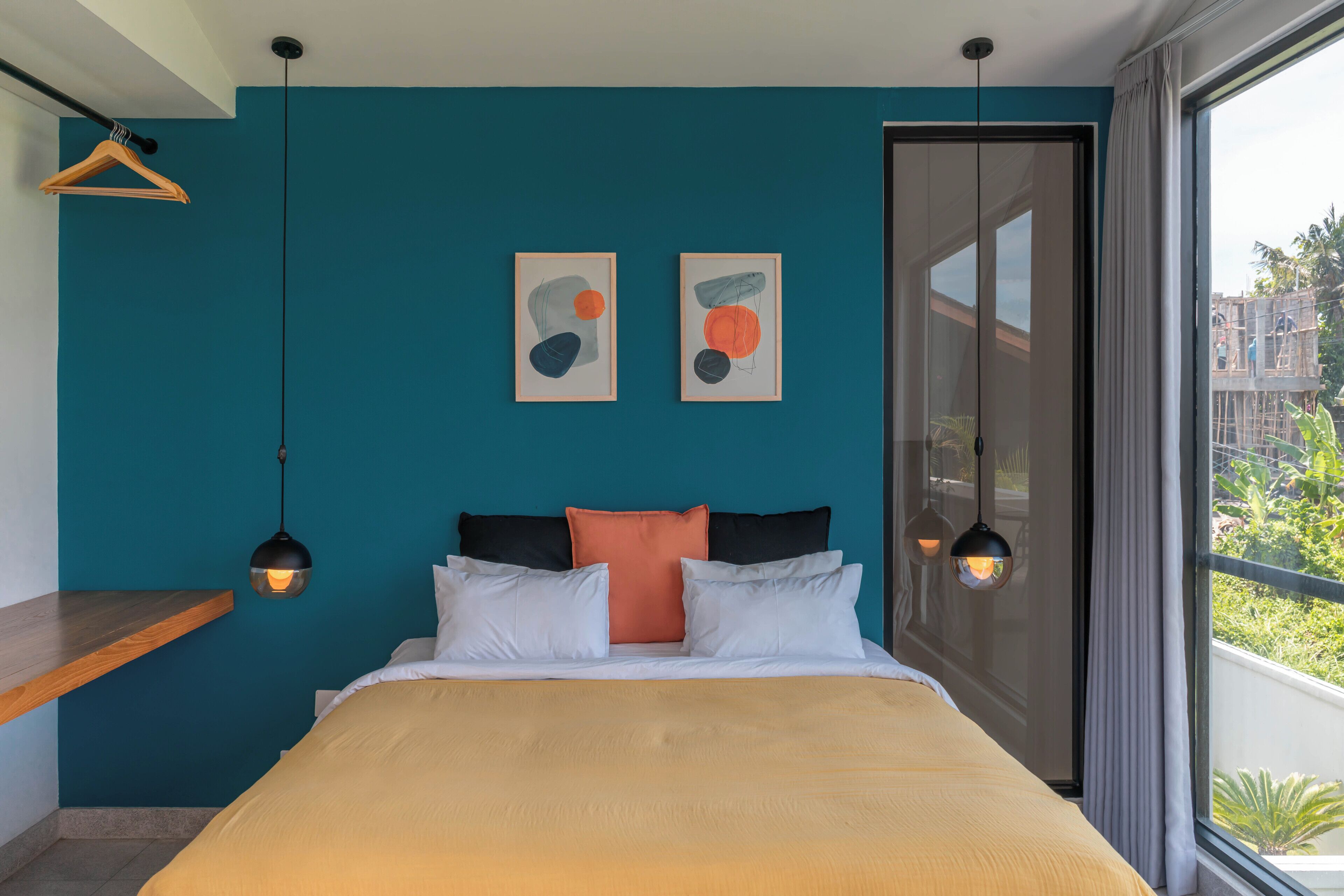Ein Schlafzimmer mit einem Bett, zwei Wandbildern, einer Pendelleuchte und Blick auf Grün.