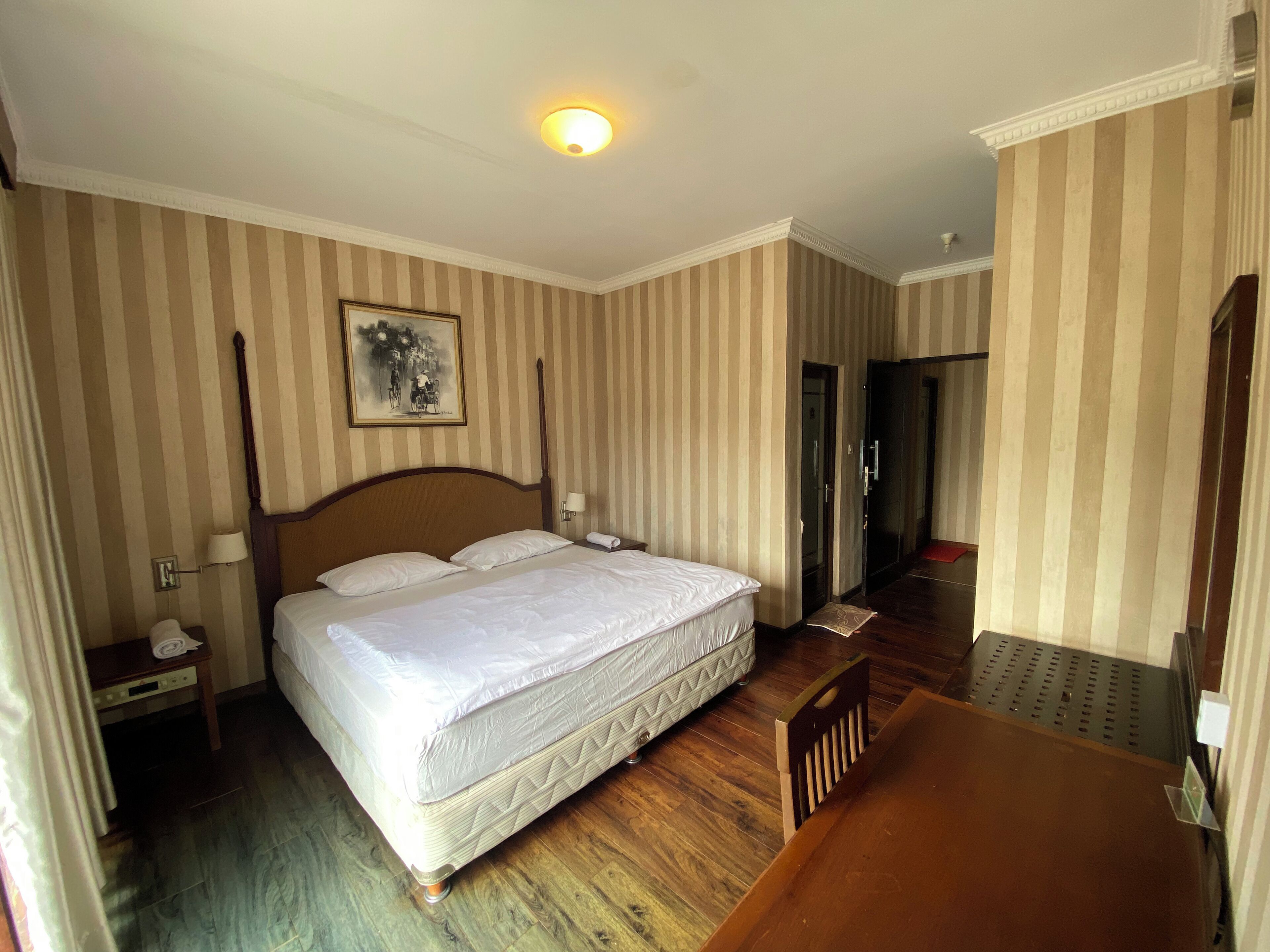 Una habitación de hotel con una cama grande, una silla de madera, un escritorio y un cuadro en la pared.