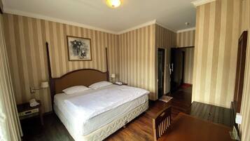 Una habitación de hotel con una cama grande, una silla de madera, un escritorio y un cuadro en la pared.