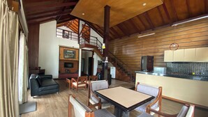 Uma sala de estar espaçosa com teto de madeira, lareira e área de jantar com cadeiras e mesa de madeira.