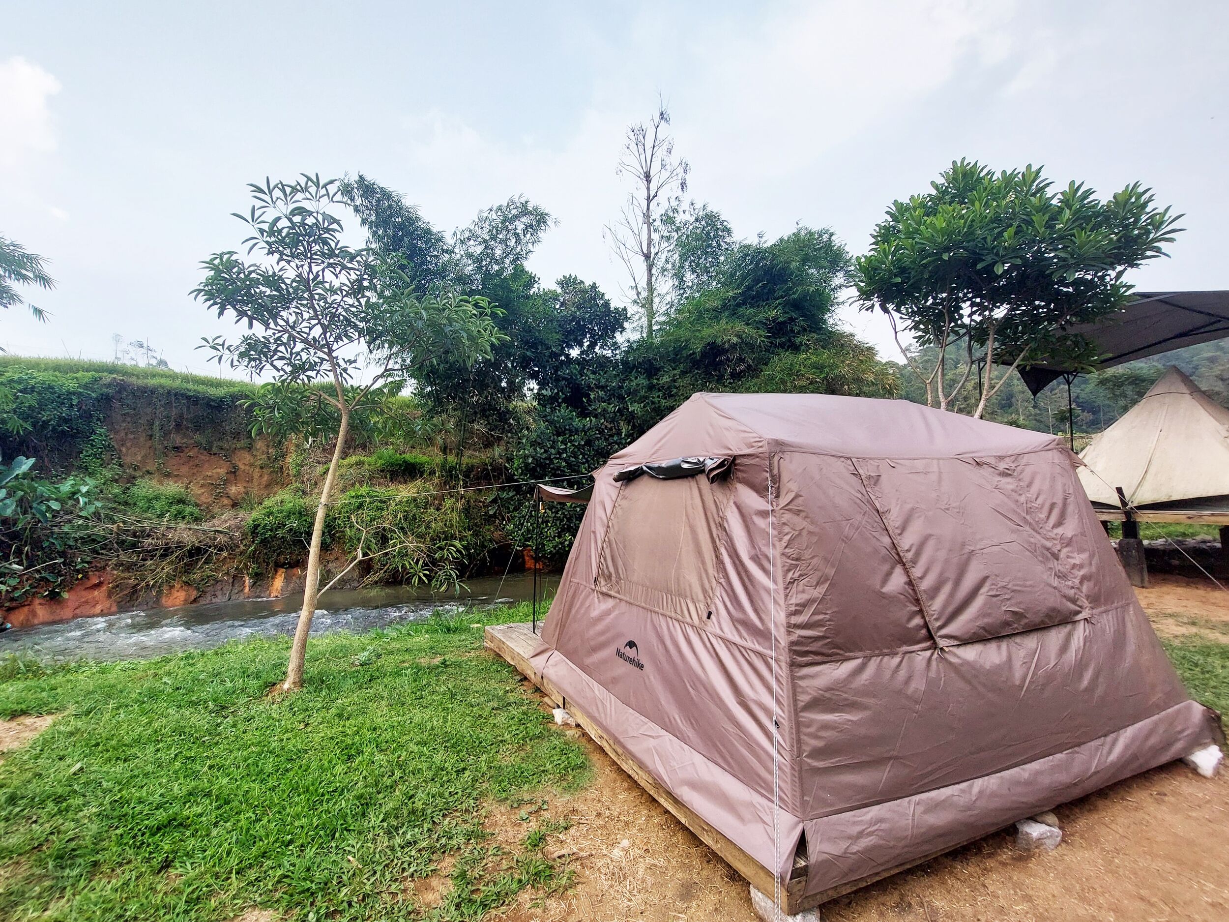 A tent set up near a river with a grassy area and trees in the background.