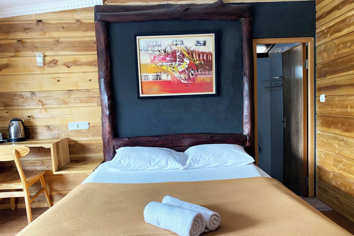 Una habitación de madera con una cama, un cuadro en la pared y un escritorio con un hervidor.