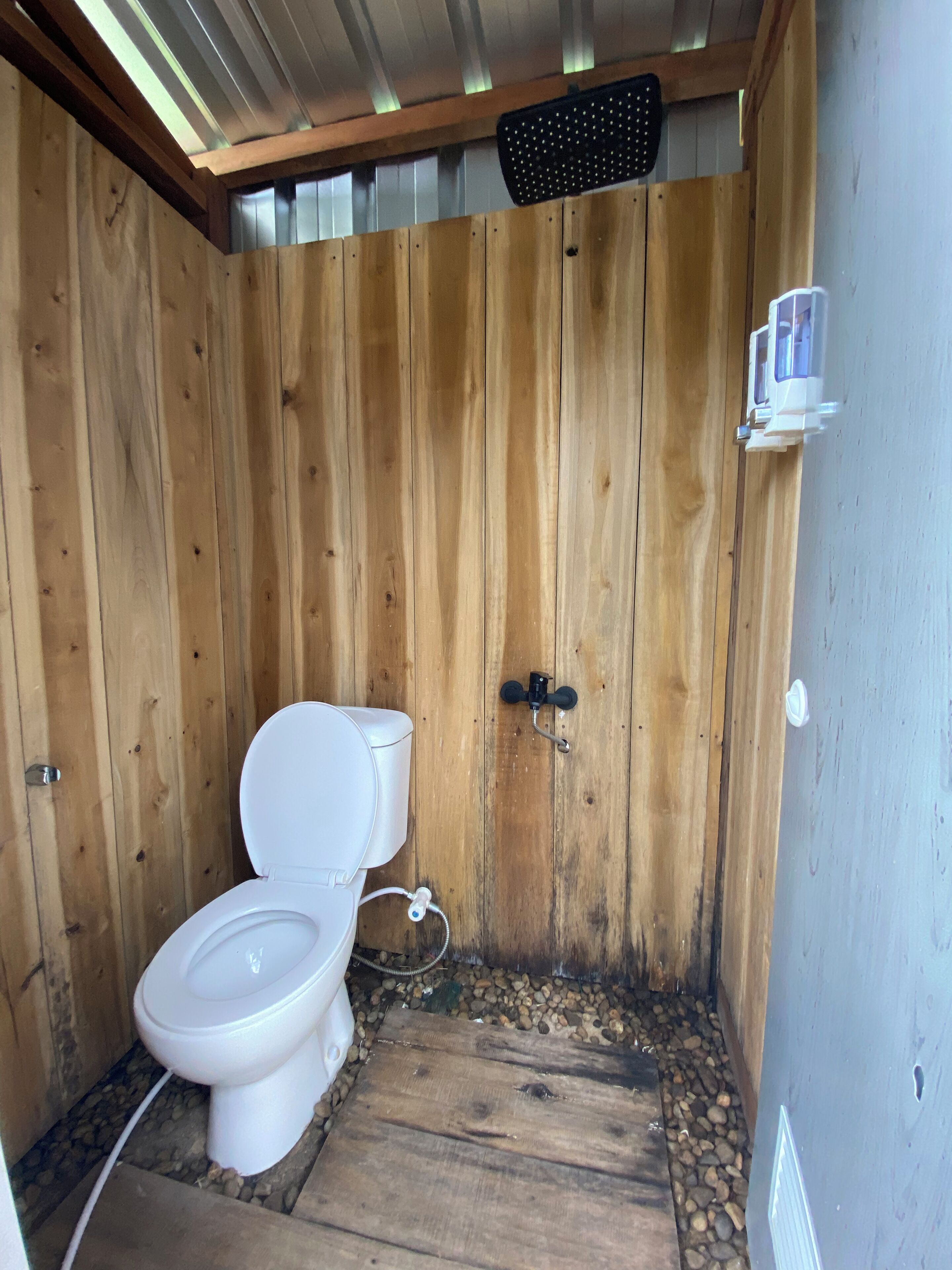 Un baño de madera con inodoro blanco, zona de ducha y un estante pequeño con artículos de aseo.