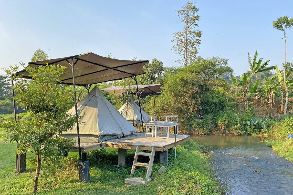 Un campamento montado con tiendas de campa ña, una mesa y un banco junto a un río.