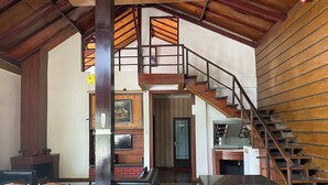 Ampla sala de estar com escada de madeira, lareira e sofá de couro preto.