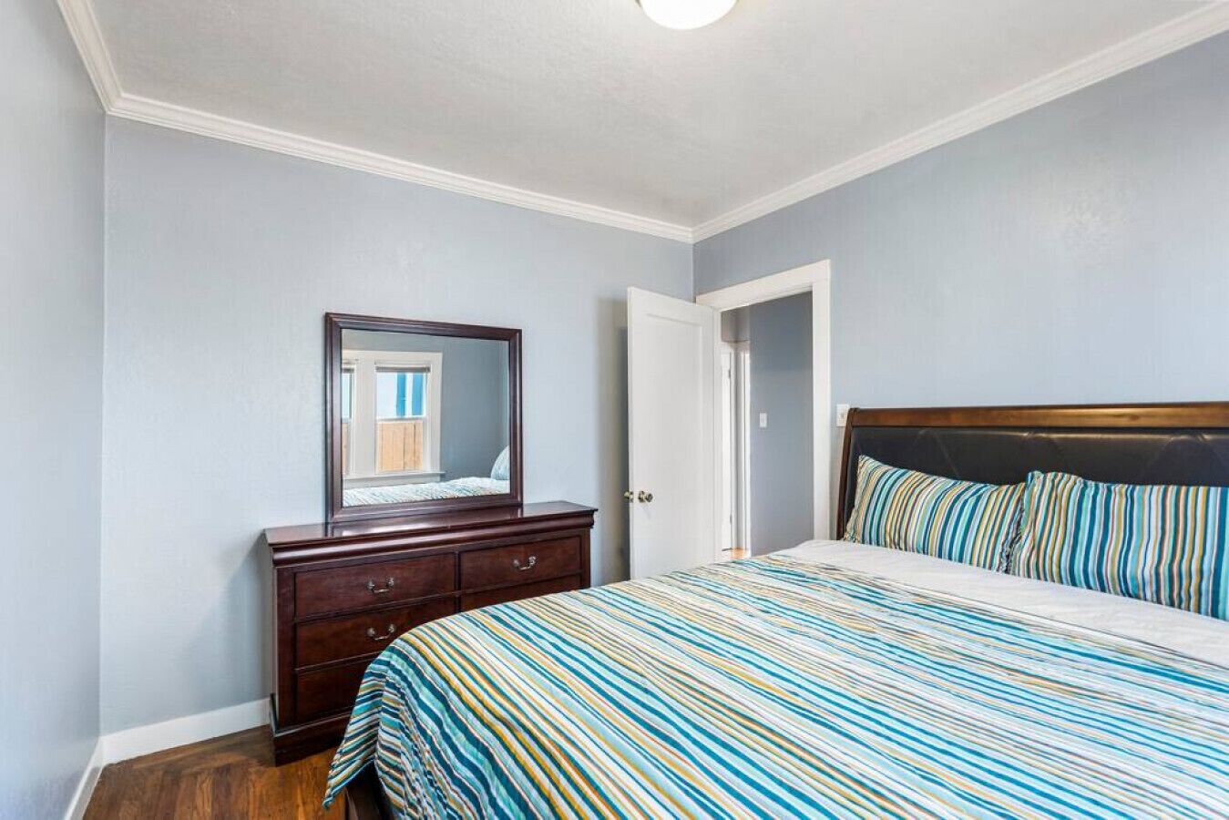Un dormitorio con cama, cómoda, espejo y puerta.