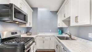 A compact kitchen with white cabinets, a stainless steel range, a microwave, and a sink.
