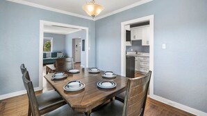 A dining area with a wooden table set for four, a chandelier, and a view into the kitchen.
