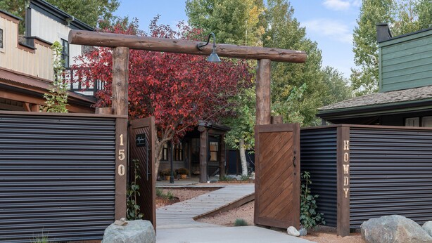 A gated entrance with a wooden archway, a metal gate, and a pathway leading to a building with a green roof. - Hotel Palomino (Ridgway)