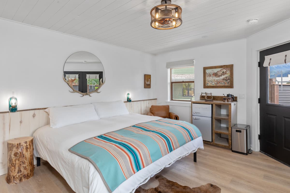 A bedroom with a large bed, a mirror, a desk, and a small trash bin.