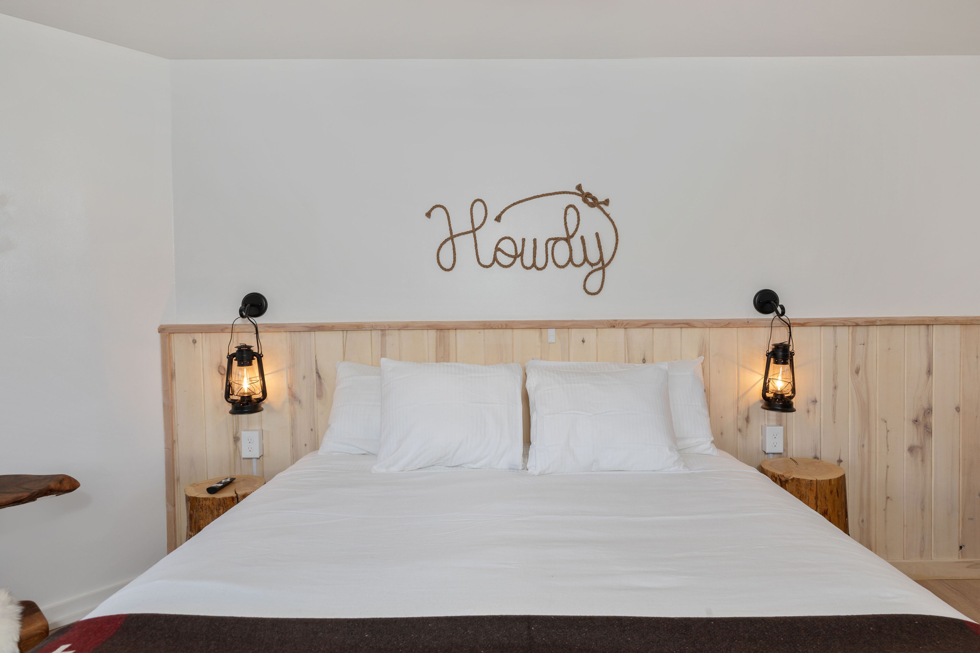 Una cama bien hecha con ropa blanca, dos mesitas de noche con lámparas tipo farol y un cabecero de madera.