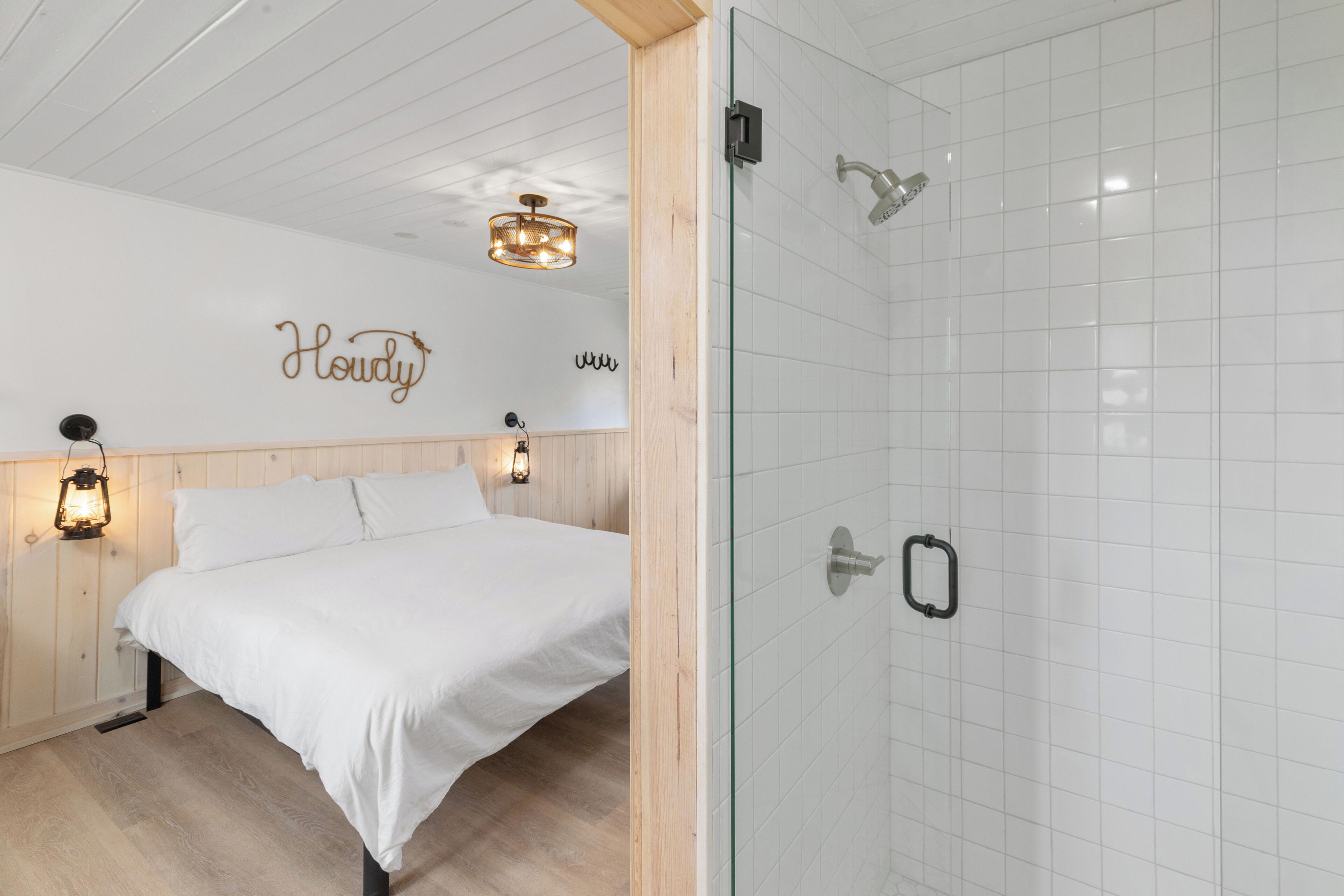 Un dormitorio con cama, mesita de noche, luz empotrada en la pared y cabina de ducha de vidrio.