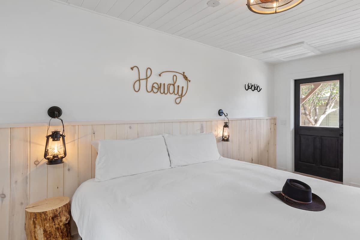 A bedroom with a bed, a wooden headboard, two wall-mounted lanterns, and a door with a window.