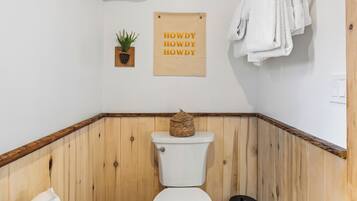 Een betegelde badkamer met een toilet, een kleine plant en een bordje met de tekst 'HOWDY HOWDY HOWDY'.