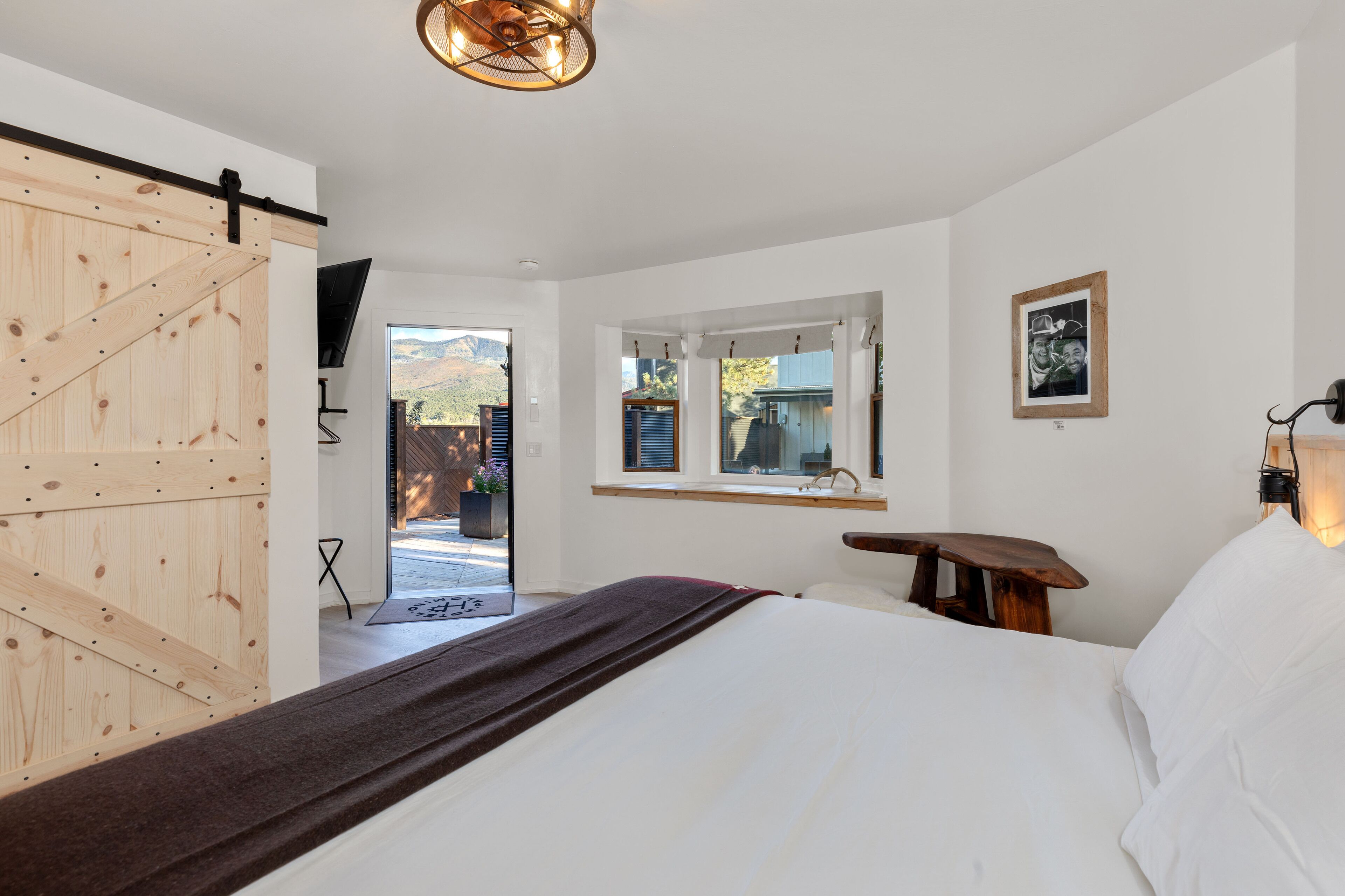 Un dormitorio con una cama grande, una puerta corredera de madera, una ventana con vistas y una lámpara fijada a la pared.