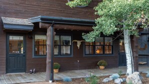 A wooden building with a dark brown exterior, a porch with a wooden railing, and a small garden area with rocks and plants. - Hotel Palomino (Ridgway)