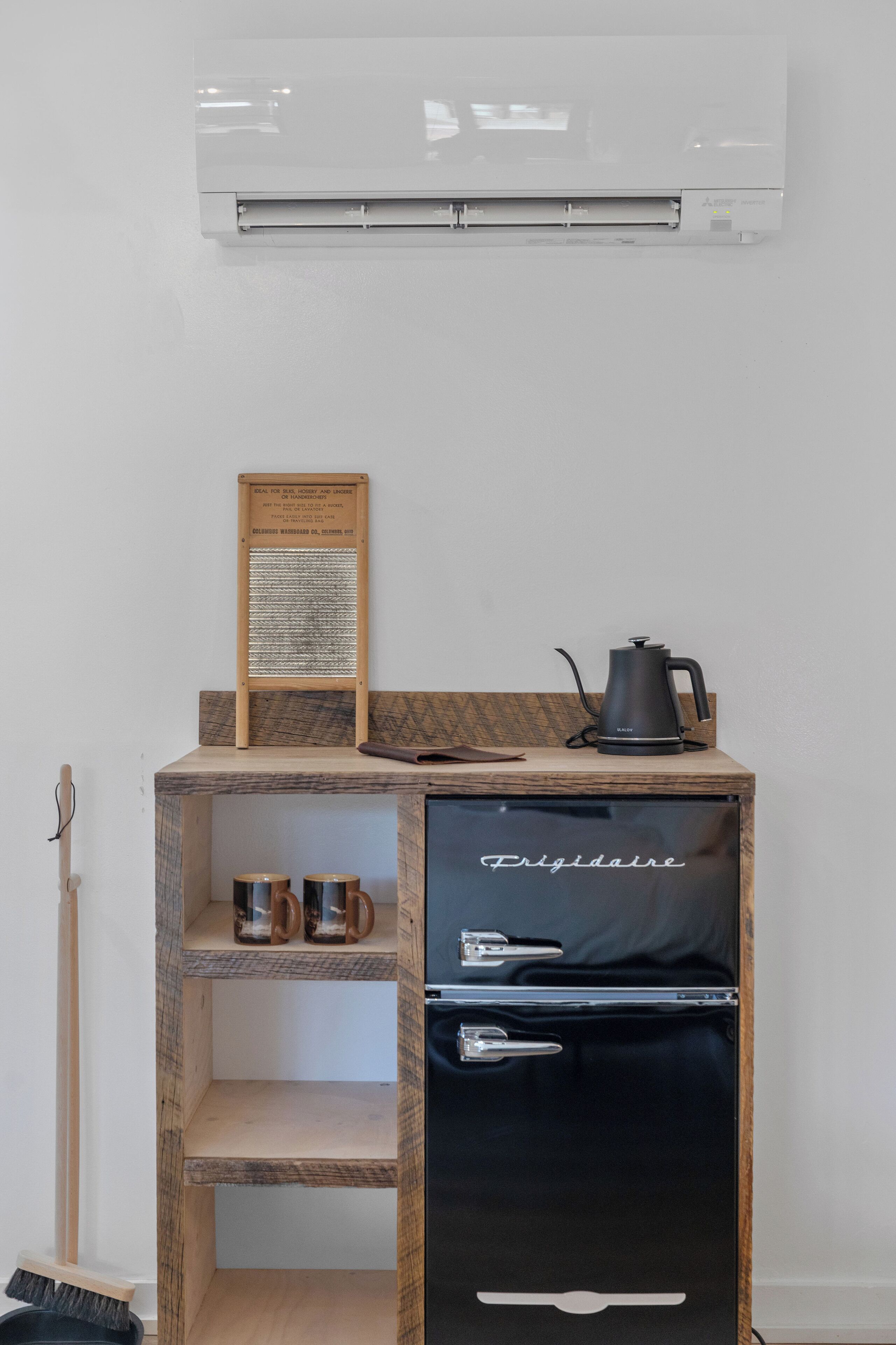 A compact kitchenette with a black refrigerator, a wooden shelf, and a coffee maker.