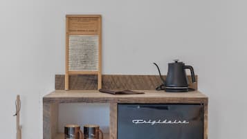 A compact kitchenette with a black refrigerator, a wooden shelf, and a coffee maker.