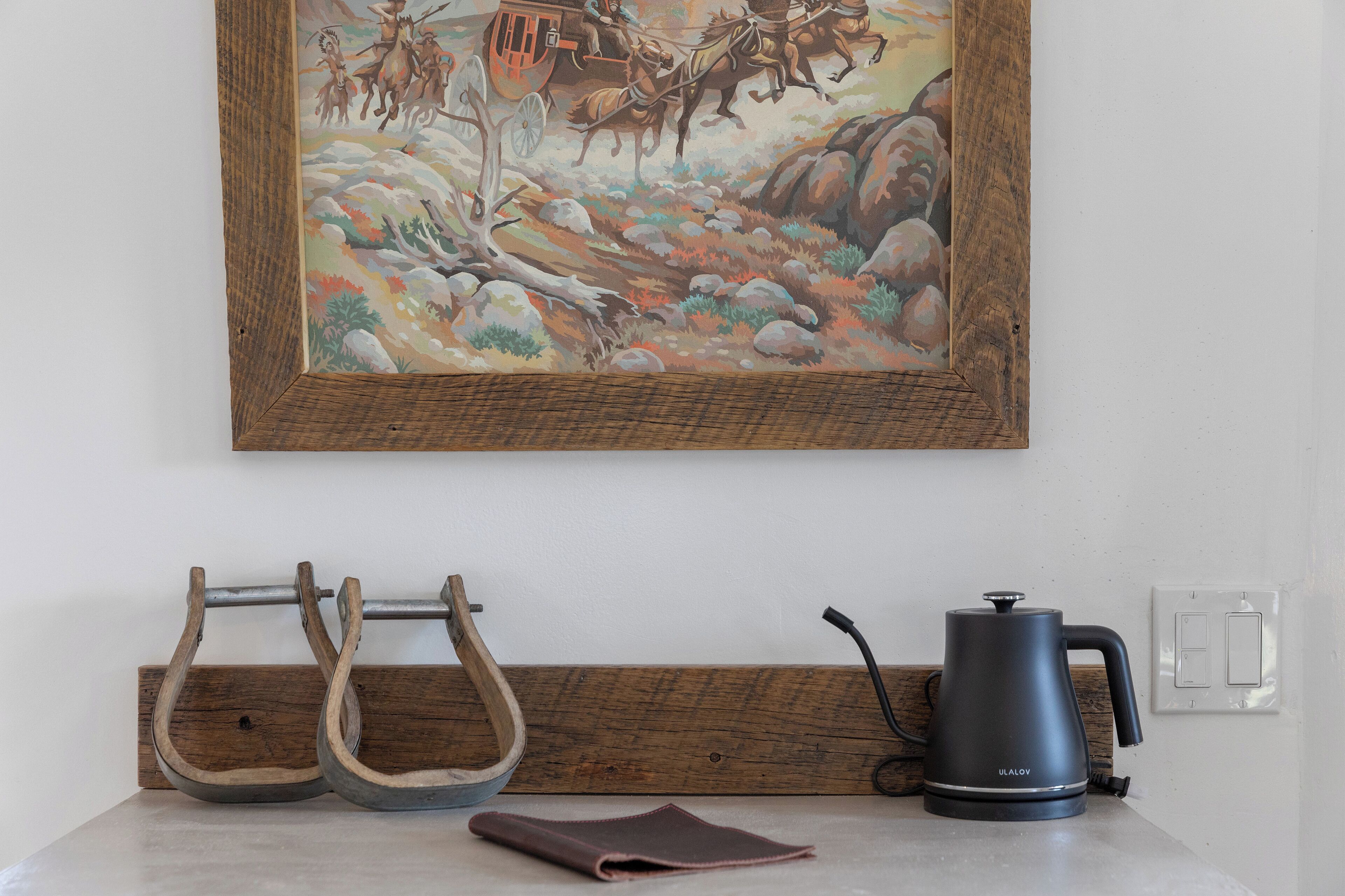 A kitchen with a wooden countertop, a kettle, and a framed painting above.
