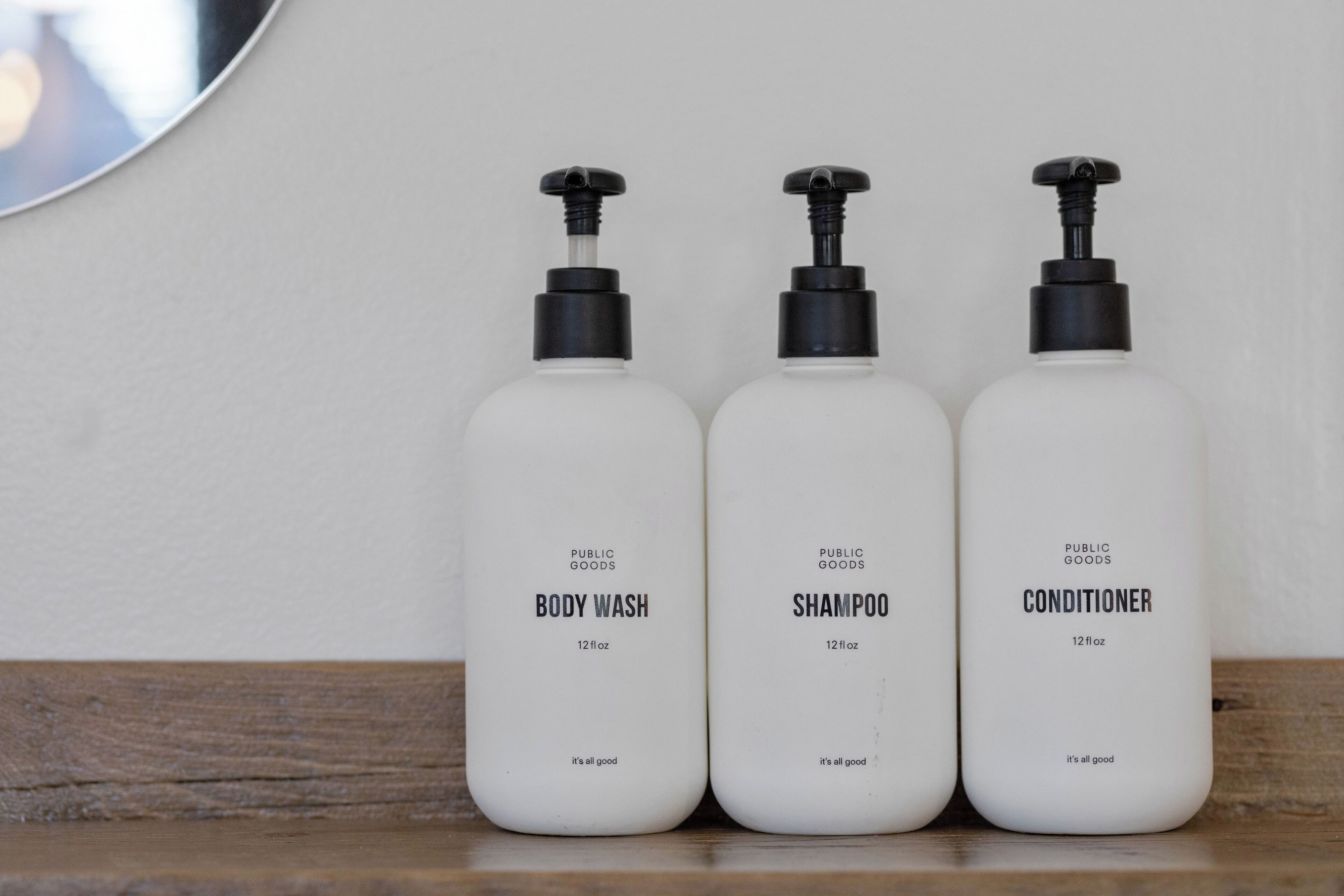 Tre flaconi di bagnoschiuma, shampoo e balsamo su un piano di legno.