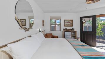 A bedroom with a large bed, a desk with a chair, a mirror, and a door leading to a balcony.