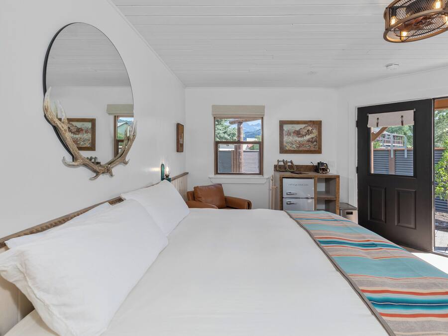 A bedroom with a large bed, a desk with a chair, a mirror, and a door leading to a balcony.