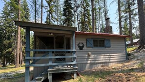 A cabin with a porch and a small deck, surrounded by tall trees. - Small waterfront cabin with private dock on beautiful McGregor Lake (Marion)