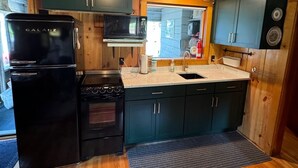 A compact kitchen with wooden cabinets, a black refrigerator, a microwave, and a stove. - Small waterfront cabin with private dock on beautiful McGregor Lake (Marion)