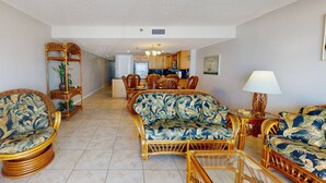A spacious living area with wicker furniture, a dining table, and a kitchen in the background.