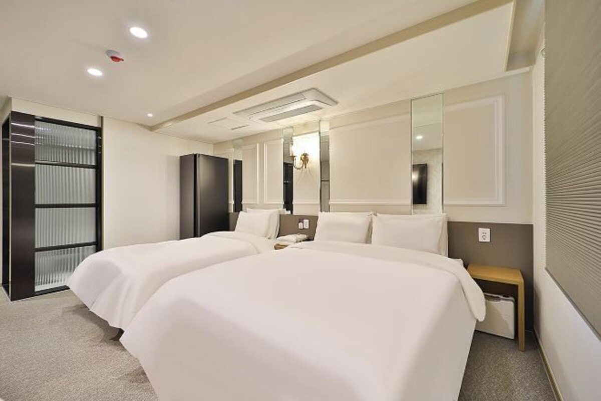 A hotel room with two beds, a large mirror, a bedside table, and a wardrobe.
