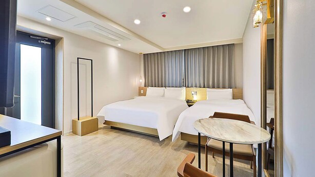Ein Hotelzimmer mit einem großen Bett, Nachttischen, einem Schreibtisch und einem kleinen runden Tisch mit Stühlen.