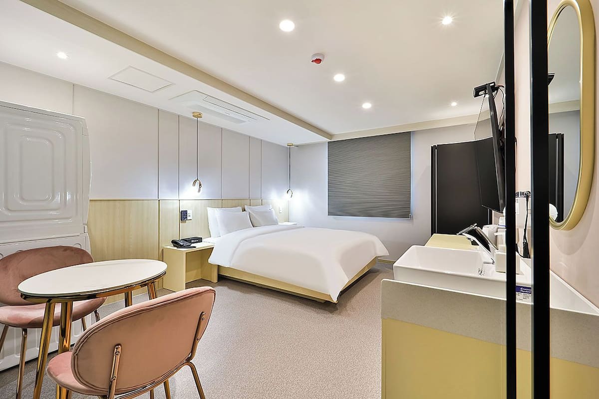 Ein Hotelzimmer mit Bett, Nachttisch, Lampe, Stuhl und Schminktisch mit Spiegel.