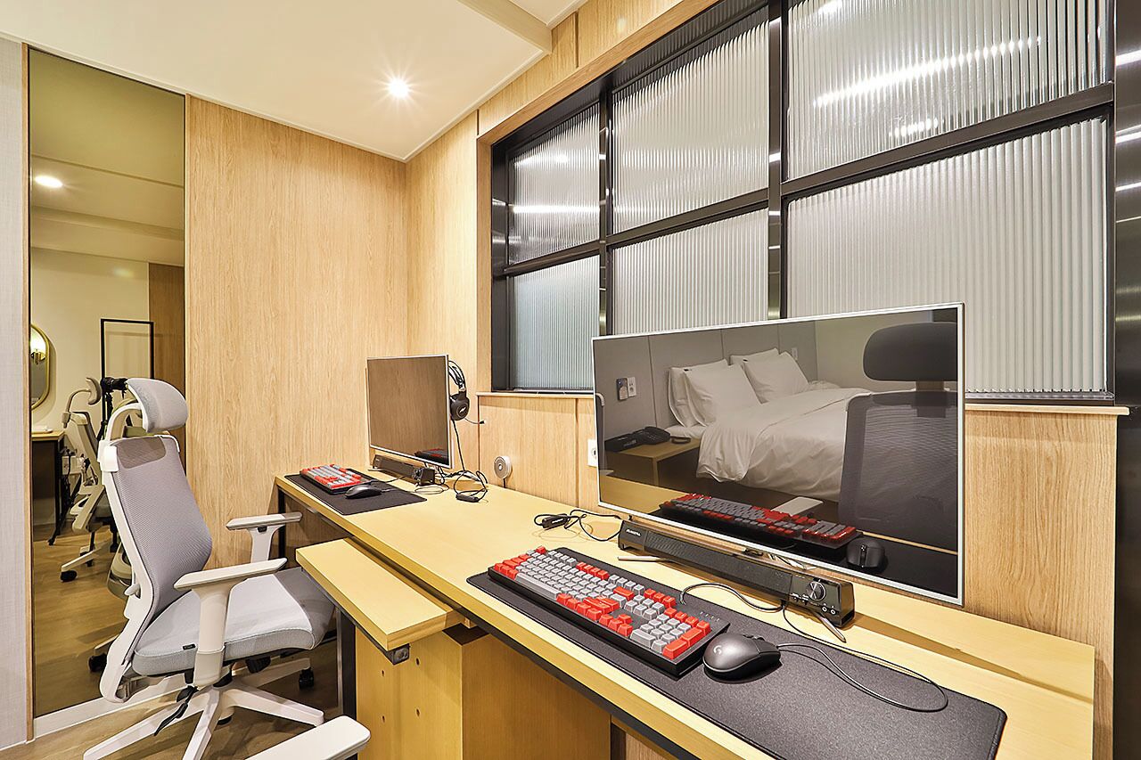 A modern hotel room with a large bed, a desk with a computer, and a chair.